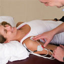 Chiropractor using electronic device on a woman lying on a bed